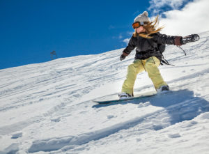 A young girl snowboards outside wearing snow gear and goggles.