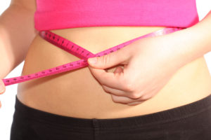 A woman measures her waist with pink measuring tape.