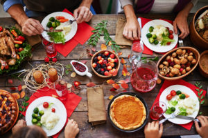 A few people gather and eat at a kitchen table filled with holiday food.