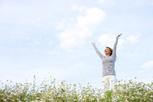 A woman stands in a field of flowers and raises her hands toward the sky.