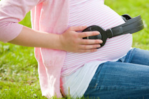 A pregnant woman places headphones on her stomach.