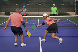 A group of four adults play pickleball.