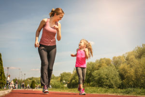 A mom jogs with her little daughter outside.