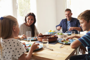 A family sits at a dinning table eating potatoes and vegetables.