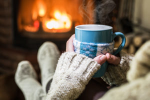 A person holds a coffee mug near a fireplace.