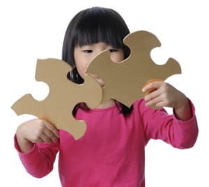A young girl places two large puzzle pieces together.