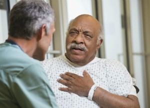 An elderly man places his hand over his heart and talks to a doctor.