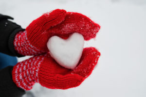 A person wearing gloves holds a heart-shaped snowball.