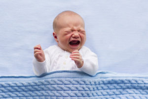 A baby is shown crying as they lie in bed.