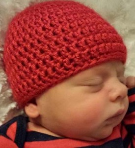 A little boy wears a red hat from Mended Little Hearts.