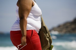 An obese woman walks along a beach.