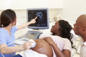 A woman lies on an exam table as she gets an ultrasound to see her baby.