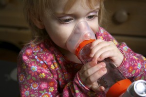 A young girl breathes into a large inhaler.