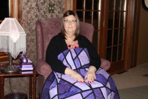 Martha Ribbens sits in a chair and places a colorful patchwork quilt on her lap.
