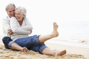 An elderly couple sits together at the beach and smiles.