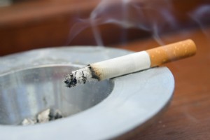 A cigarette sits in an ash tray.