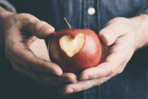 A man holds a red apple. The apple has a heart-shaped cut on it.