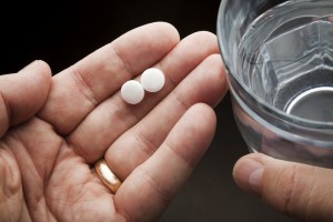 A person holds two pills of aspirin in one hand and a glass of water in the other hand.
