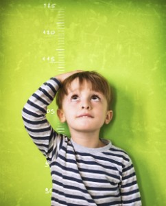 A child measures his height up against a green wall.