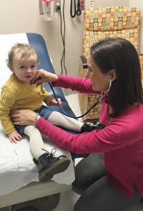 Giselle Saulnier Sholler, MD, and her little patient, Erica, from Ireland, are shown in an exam room.