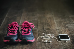 A cellphone with headphones are shown placed next to a pair of black-and-pink tennis shoes.
