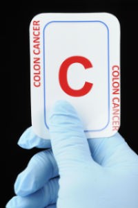 A person wearing a medical glove holds a card that says, "Colon Cancer."