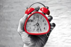 A person holds a mini red alarm clock in their hand.