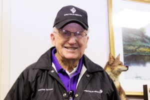 Bob Gill, 93, poses for a photo. Bob wears a Spectrum Health hat and jacket.