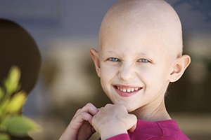 A young girl poses for a photo. She is bald and smiling.
