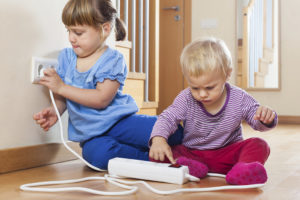 Two little kids playing with electrical outlets.