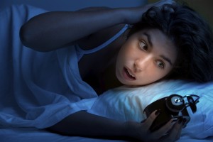 A young woman looks at her alarm clock while she lies in bed. 