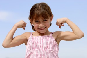 A young girl flexes her arms and smiles.