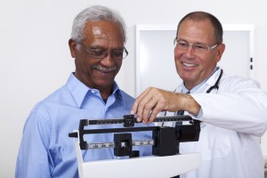 An older man gets his weight measured by a medical professional.