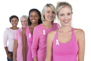 A group of women pose for a photo together. They all wear pink shirts with a breast cancer ribbon on it.