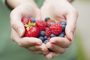 A woman holds blueberries, strawberries and raspberries in her hands.