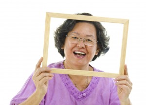 A woman holds an empty picture frame in front of her face and smiles.