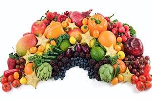 A group of fruit and vegetables are shown shaped into a color-coordinated rainbow.