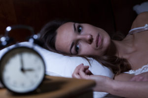 A woman lies in bed and looks at her alarm clock.
