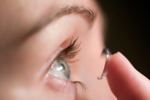 A person places a contact lens in their eye.