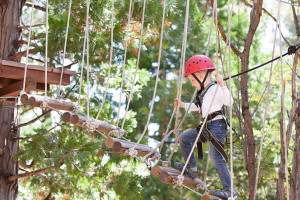 A young girl holds onto ropes while she walks through an outdoor rope course.