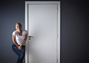 A woman holds her bladder and waits outside a restroom.