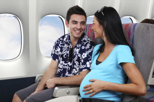 A pregnant woman sits on an airplane and smiles toward a man who sits next to her.