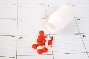 A pill bottle spills out a few pills onto a calendar.