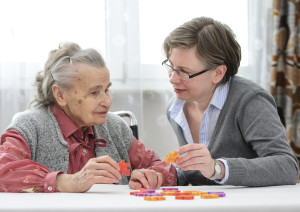 An elder care nurse works on a jigsaw puzzle with a senior woman in a nursing home.