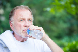 A man drinks a bottle of water as he sits outside.