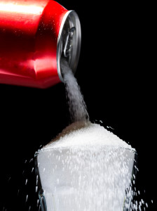 A soda can pours out sugar into a glass.