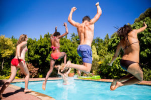 Four teens in swimsuits jump into a swimming pool.