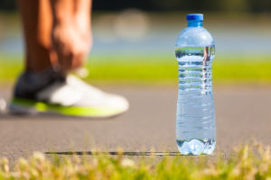 A runner ties their tennis shoes next to a water bottle outside.