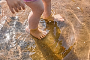 A young girl puts her feet in the water at the beach.