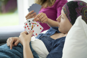 A person lies in a hospital bed an plays a card game with a visitor.